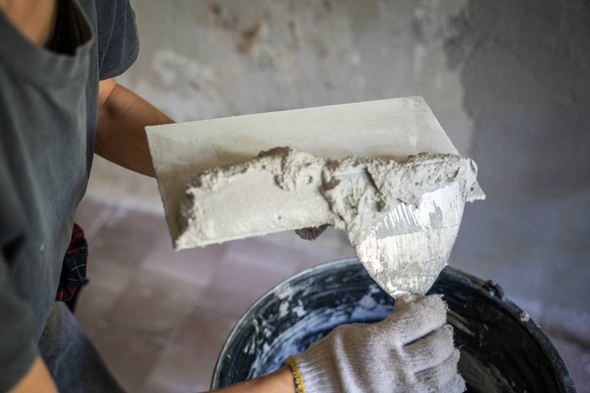 A gloved hand adds plaster to a trowel using a trowel, close-up.