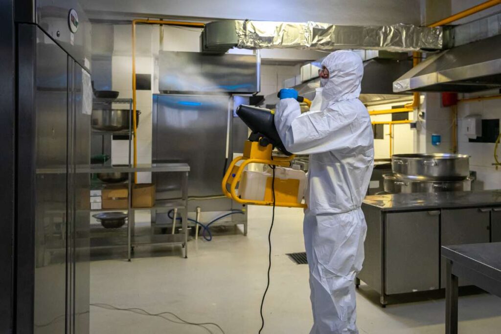 man in protective equipment disinfects with a spray gun industrial kitchen surfaces due to coronavirus covid-19 .Virus pandemic