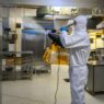 man in protective equipment disinfects with a spray gun industrial kitchen surfaces due to coronavirus covid-19 .Virus pandemic