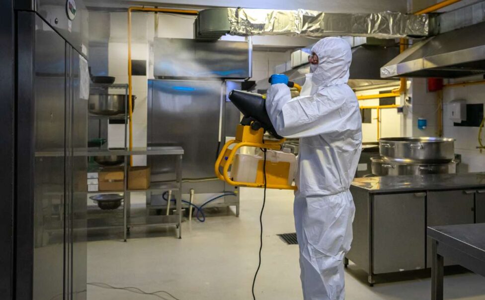 man in protective equipment disinfects with a spray gun industrial kitchen surfaces due to coronavirus covid-19 .Virus pandemic